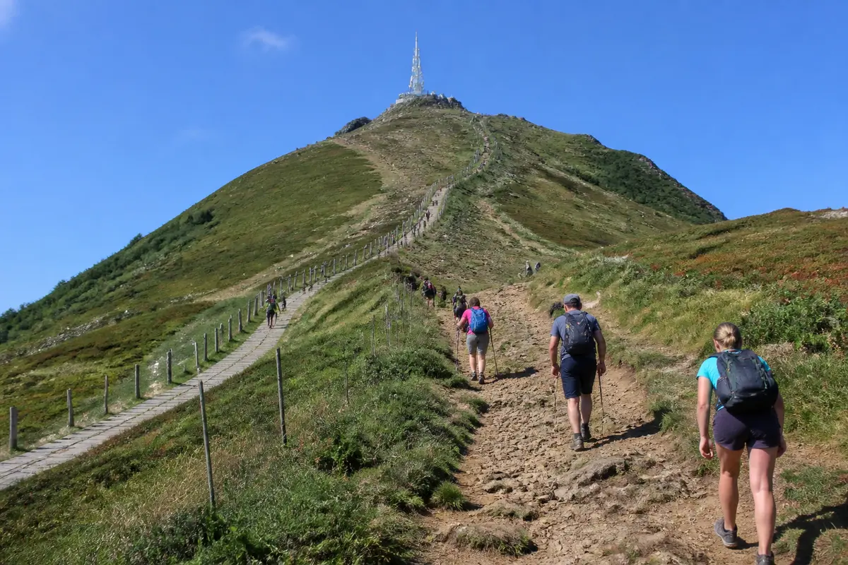 Randonneurs sur le sentier de l'ascension du Puy de Dôme sous un ciel bleu