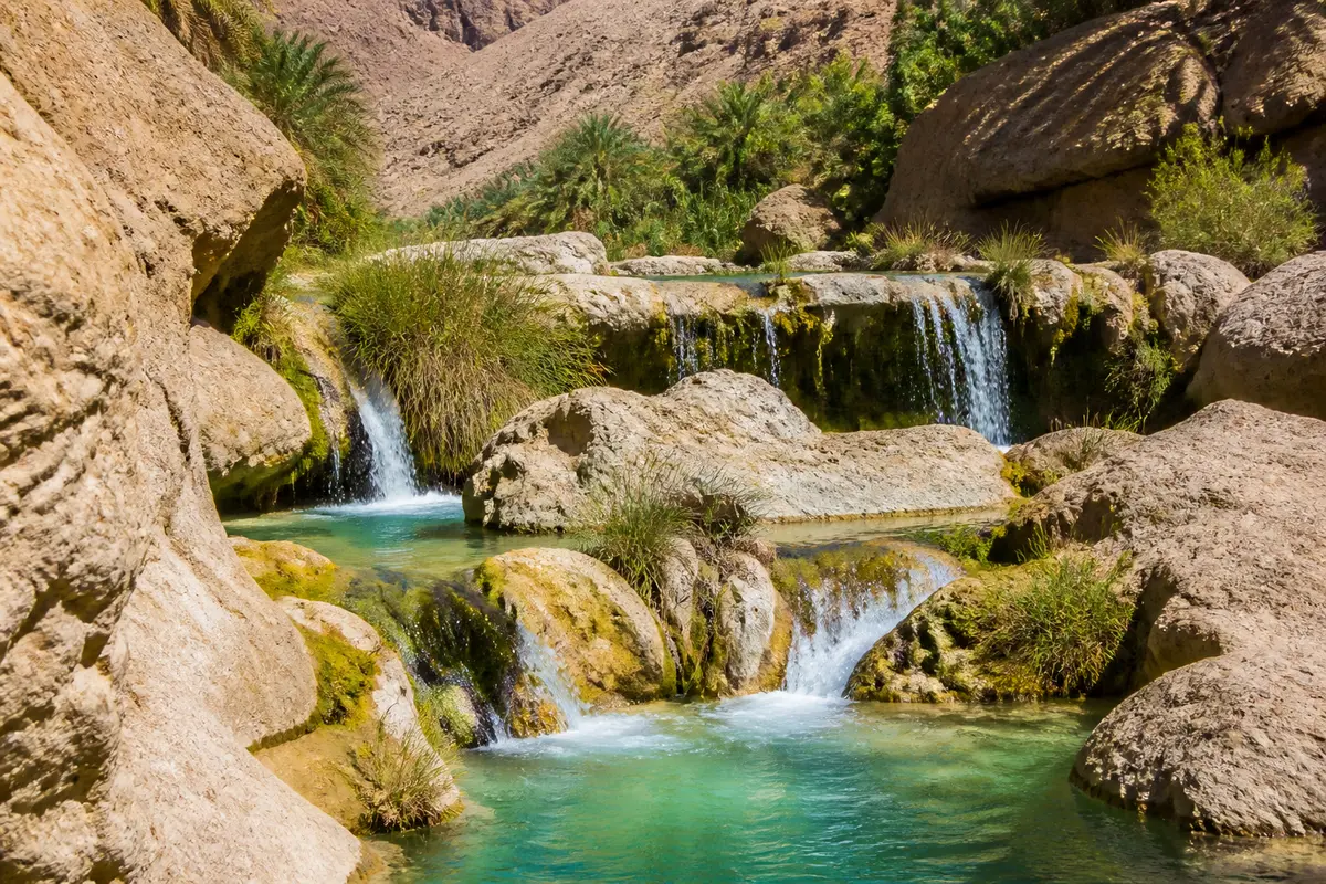 Cascade dans un wadi omanais entourée de rochers et palmiers verdoyants